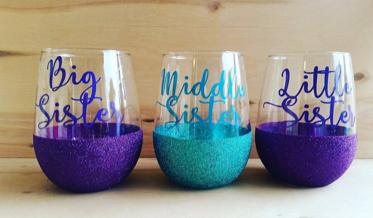 big sister in purple text on stemless wine glass with purple glitter to half line, middle sister in teal text on stemless wine glass with teal glitter to half line, little sister in purple text on stemless wine glass with purple glitter to half line
