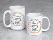 love never fails corinthians 13:8 quote in peach or olive with peach and olive floral wreath on ceramic mug on 2 mug sizes