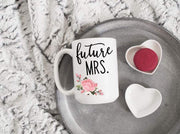 future mrs. in black text with pink and green floral bottom left printed coffee mug laid down with ceramic hear and macaroons