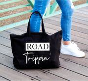 Road trippin' white words on large black tote bag next to womans leg